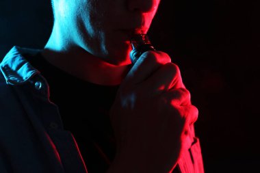 Siyah arka planda neon lambalarda elektronik sigara içen adam, yakın plan
