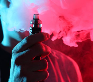 Karanlık arka planda neon lambalarda elektronik sigara içen adam, yakın plan