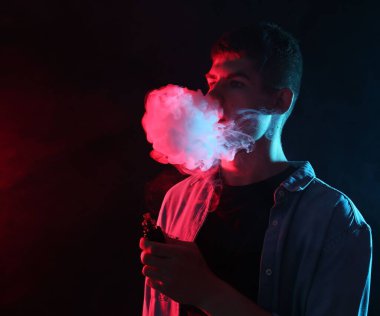 Koyu arkaplanda neon lambalarda elektronik sigara içen adam, metin için boşluk