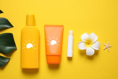 Güneş kremi ürünleri, tesisat çiçeği, yeşil yaprak ve deniz yıldızı sarı arka planda, üst manzara. Güneş resimli şişe ve tüp