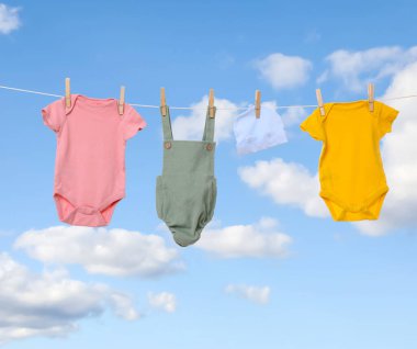 Mavi gökyüzüne karşı çamaşır ipinde kurumuş farklı bebek kıyafetleri.