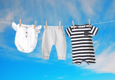 Mavi gökyüzüne karşı çamaşır ipinde kurumuş farklı bebek kıyafetleri.