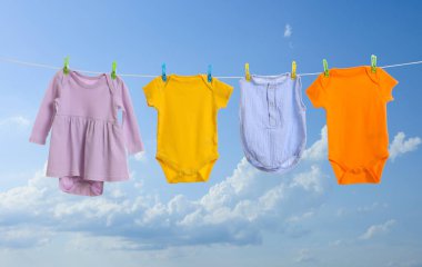 Mavi gökyüzüne karşı çamaşır ipinde kurumuş farklı bebek kıyafetleri.