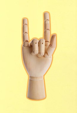 Tahta manken elinde soluk sarı arka planda kaya jesti var.