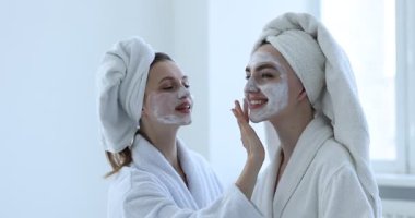 Bornozlu mutlu bir kadın, kaplıca ameliyatından sonra arkadaşına yüz maskesi takıyor.