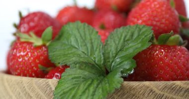 Beyaz arka planda yeşil yapraklı taze olgun çilekler dönüyor.