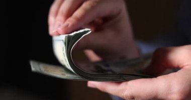 Karanlık arka planda para sayan bir kadın, yakın plan.