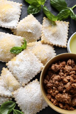 Pişmemiş ravioli, bolonez ve fesleğen siyah masada, düz yerde.