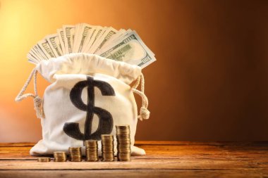 Dolar banknotları ve ahşap masanın üzerine yığılmış bozuk paralarla kahverengi gradyan arkaplan, metin için boşluk