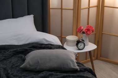 Çalar saati olan yan masa ve yatağın yanındaki dekor.