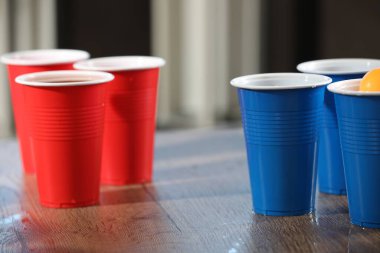 Bira pong oyunu. İçkili plastik bardaklar ve tahta masada top, yakın plan.