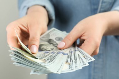 Açık gri arka planda dolar banknotları sayan kadın, yakın plan