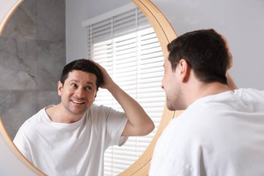 Yakışıklı adam aynada kendine bakıyor.