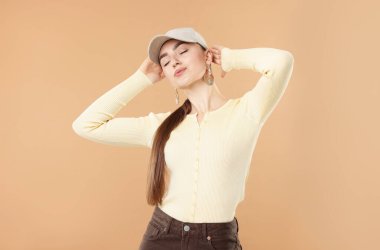 Beyzbol şapkalı güzel bir kadın bej arka planda poz veriyor.