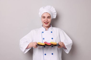 Üniformalı şekerci açık gri arka planda lezzetli ekinler tutuyor.