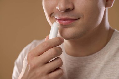 Genç adam dudaklarına krem sürüyor açık kahverengi arka planda, yakın plan.