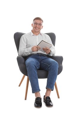 Elinde not defteri olan gülümseyen psikolog beyaz arka planda koltukta oturuyor.