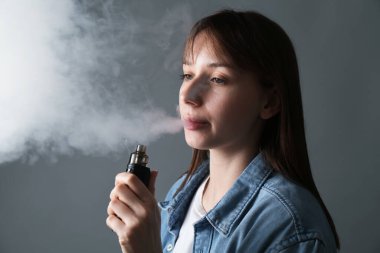 Gri arka planda elektronik sigara içen kadın
