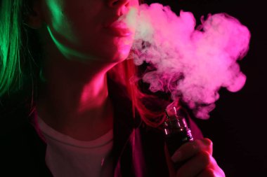 Siyah arka planda neon lambalarda elektronik sigara içen kadın, yakın plan