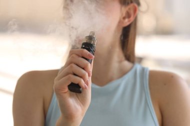 Dışarıda elektronik sigara içen genç bir kadın, yakın plan.