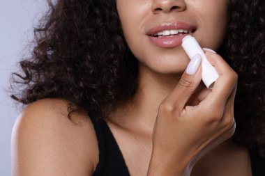 Gülümseyen kadın gri arka planda dudaklarına merhem sürüyor.