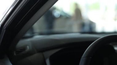 Elinde dosya olan satıcı salonda yeni bir adama yeni bir araba gösteriyor. Kamera hareket ediyor.