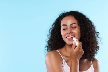 Gülümseyen kadın açık mavi arka planda dudaklarına merhem sürüyor. Metin için boşluk