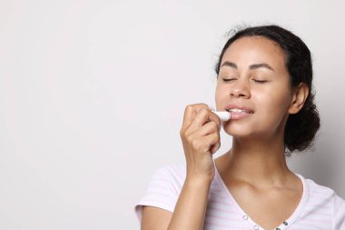 Gülümseyen kadın gri arka planda dudaklarına merhem sürüyor. Metin için boşluk