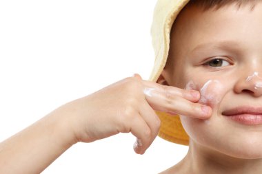 Küçük çocuk beyaz arka planda cildine güneş kremi sürüyor.