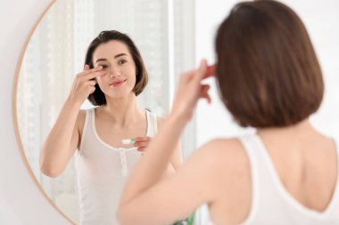 Kadın içeride aynanın yanına lens takıyor.