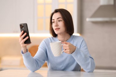 Mutfaktaki masada modern akıllı telefon kullanan bir kadın.