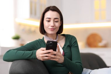 Evdeki koltukta modern akıllı telefon kullanan bir kadın.