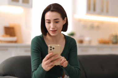 Evdeki koltukta modern akıllı telefon kullanan bir kadın.