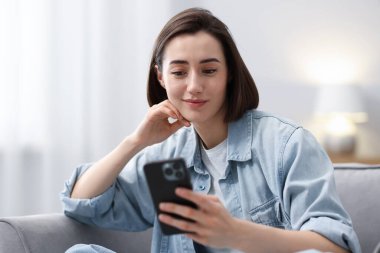 Evdeki koltukta modern akıllı telefon kullanan bir kadın.