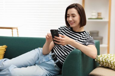 Evdeki koltukta modern akıllı telefon kullanan bir kadın. Metin için boşluk