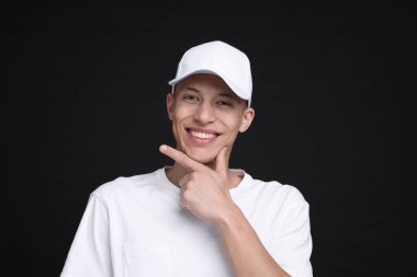 Siyah arka planda şık beyaz beysbol şapkası giyen genç bir adam.