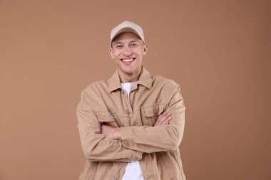 Açık kahverengi arka planda bej renkli beysbol şapkası giyen genç bir adam.