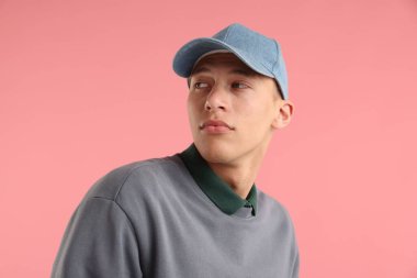 Pembe arka planda şık bir beyzbol şapkası takan genç adam.