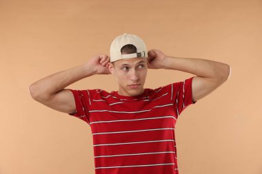 Beyzbol şapkalı genç adam bej arka planda.