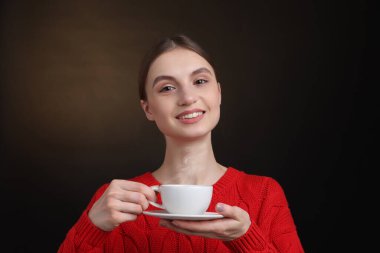 Kahverengi arka planda bir fincan kahveyle gülümseyen kadın.