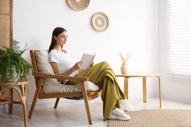 Evdeki rahat koltukta kitap okuyan güzel bir kadın.