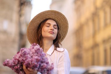 Şapkalı güzel bir kadın ve açık havada bir demet leylak çiçeği. Metin için boşluk