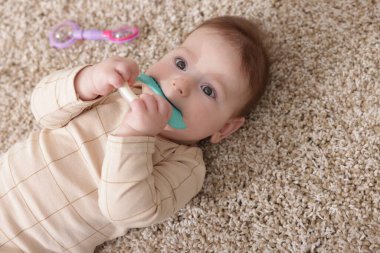 Evinin zemininde çıngıraklı oyuncağı olan sevimli bir bebek.