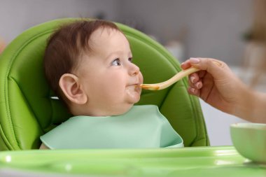 Anne bebeğini sandalyeyle besliyor, yakın plan.