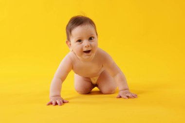 Sarı arka planda emekleyen sevimli küçük bebek.