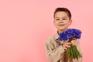 Pembe arka planda bir buket güzel çiçekle gülümseyen küçük çocuk. Metin için boşluk