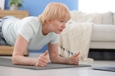 Spor giyim bölümündeki son sınıf kadın evde kalas egzersizi yapıyor, mesaj için yer var.