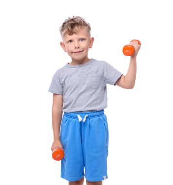 Küçük çocuk beyaz arka planda dambıllarla egzersiz yapıyor.