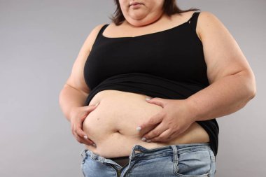 Gri arka planda aşırı göbek yağlı kadın, yakın plan.