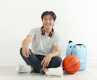 Kapalı alanda basketbol topu ve sırt çantası olan mutlu bir öğrenci.